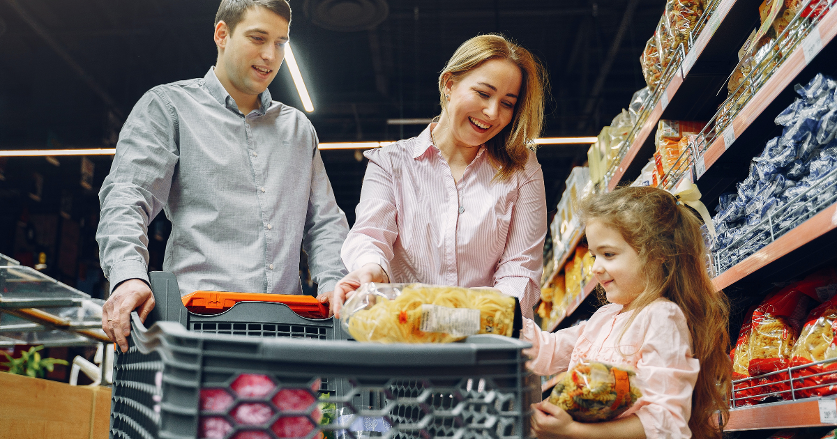 man, woman and young girl shopping in grocery store with a shopping cart